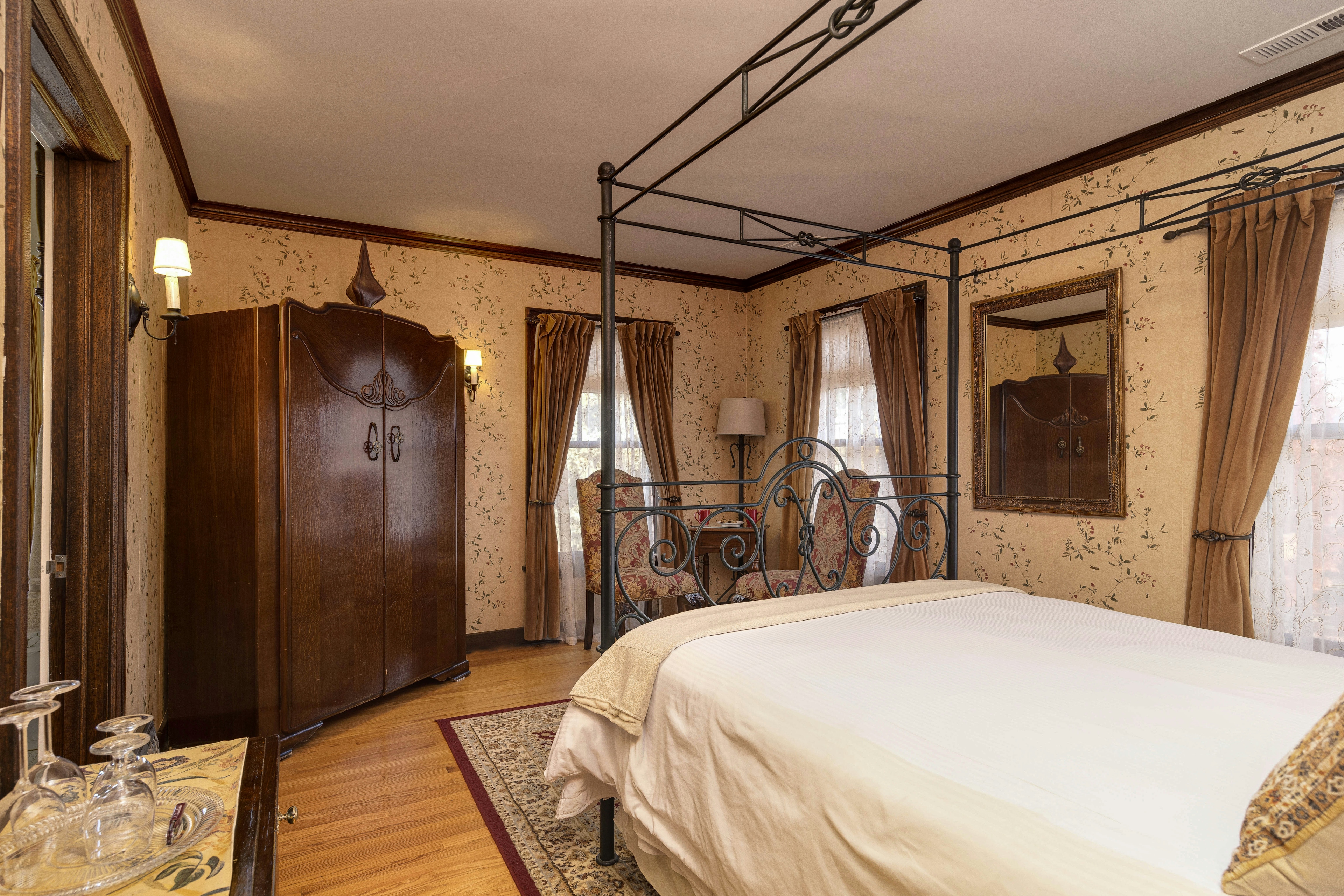 A cozy bedroom corner with two floral armchairs, a small wooden table, and curtained windows.