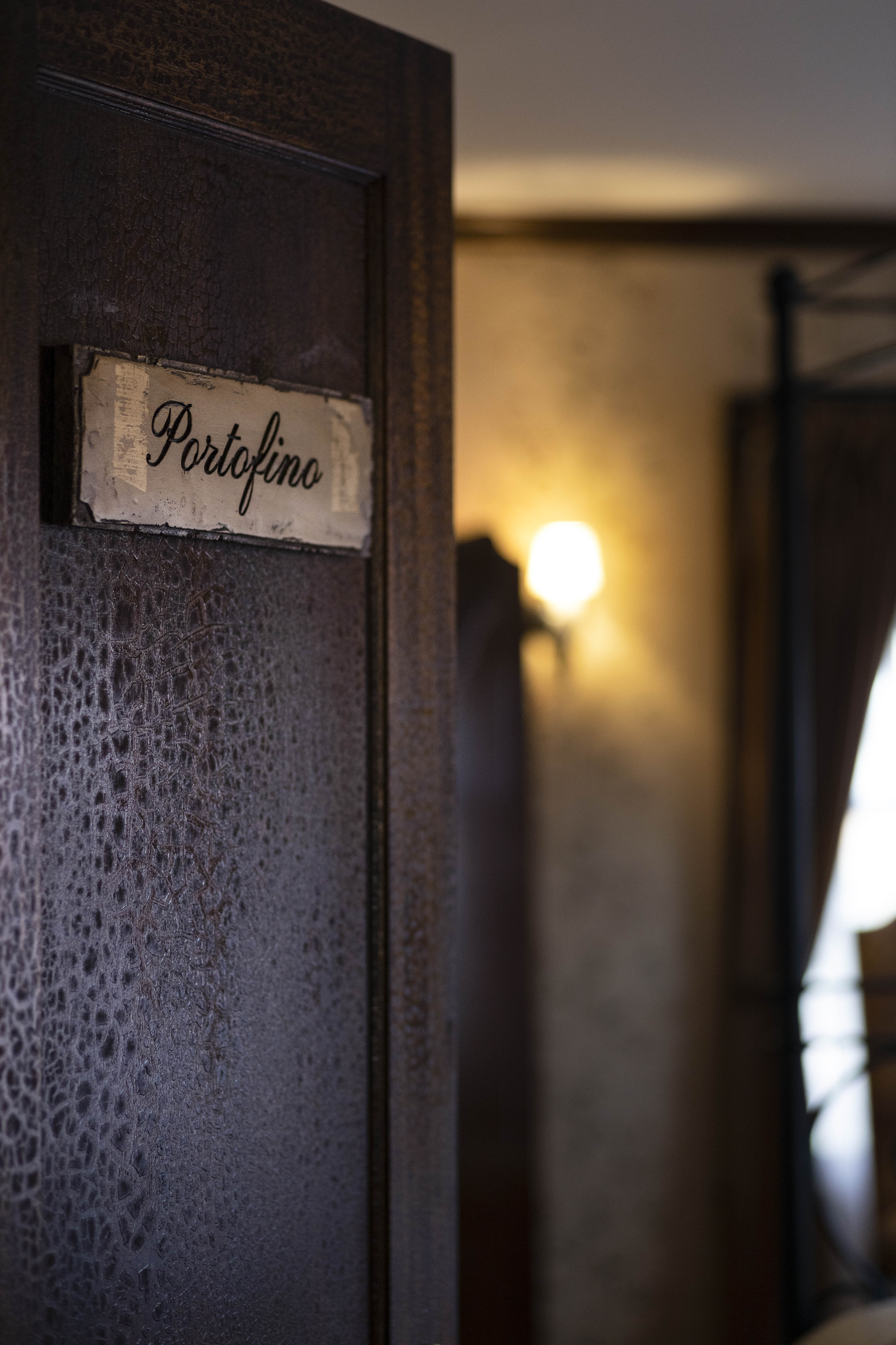 A dark wooden door with a "Portofino" sign, partially open, revealing a warmly lit room.