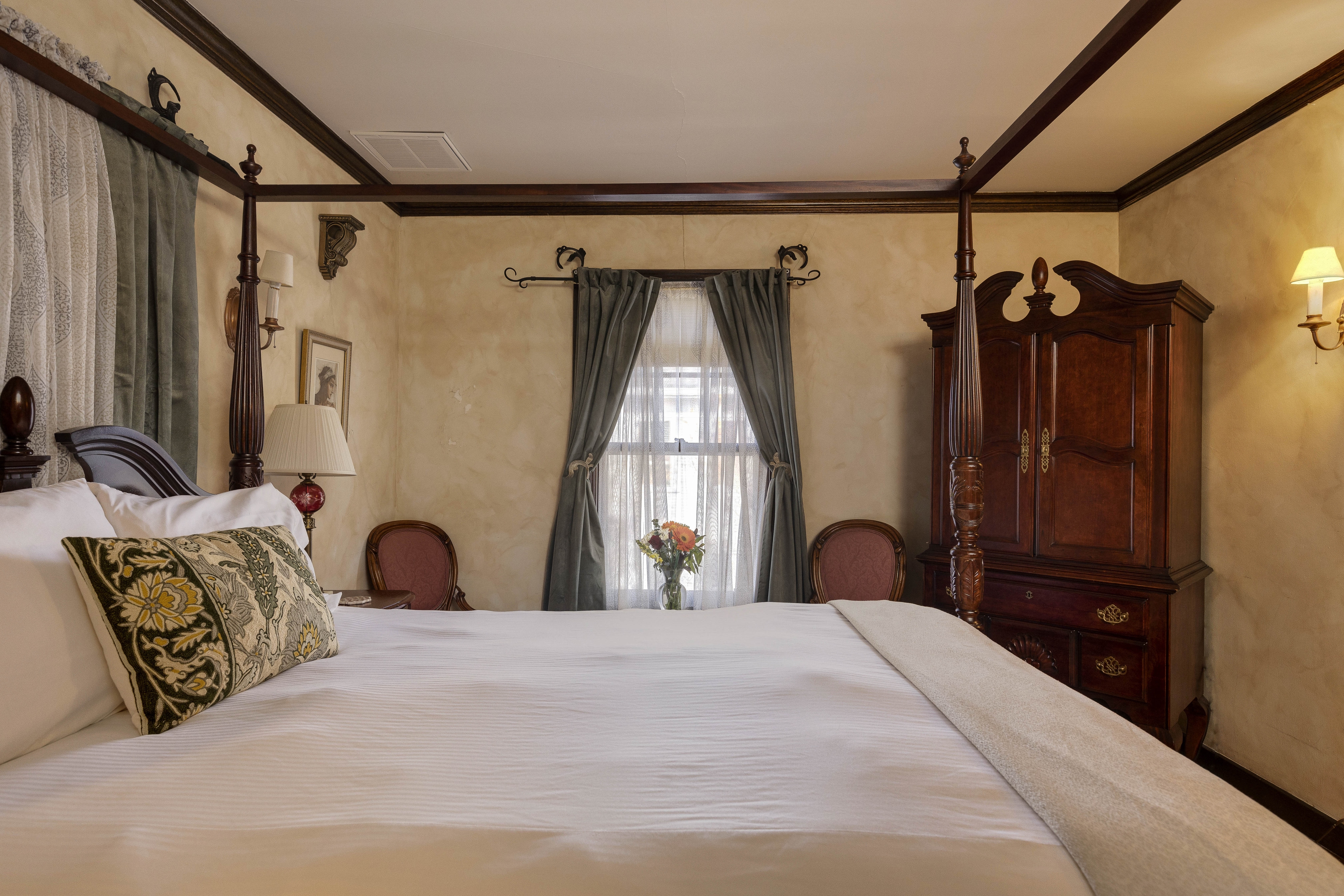 A close-up of the Napoli Guest Room bed with floral pillows and soft linens.