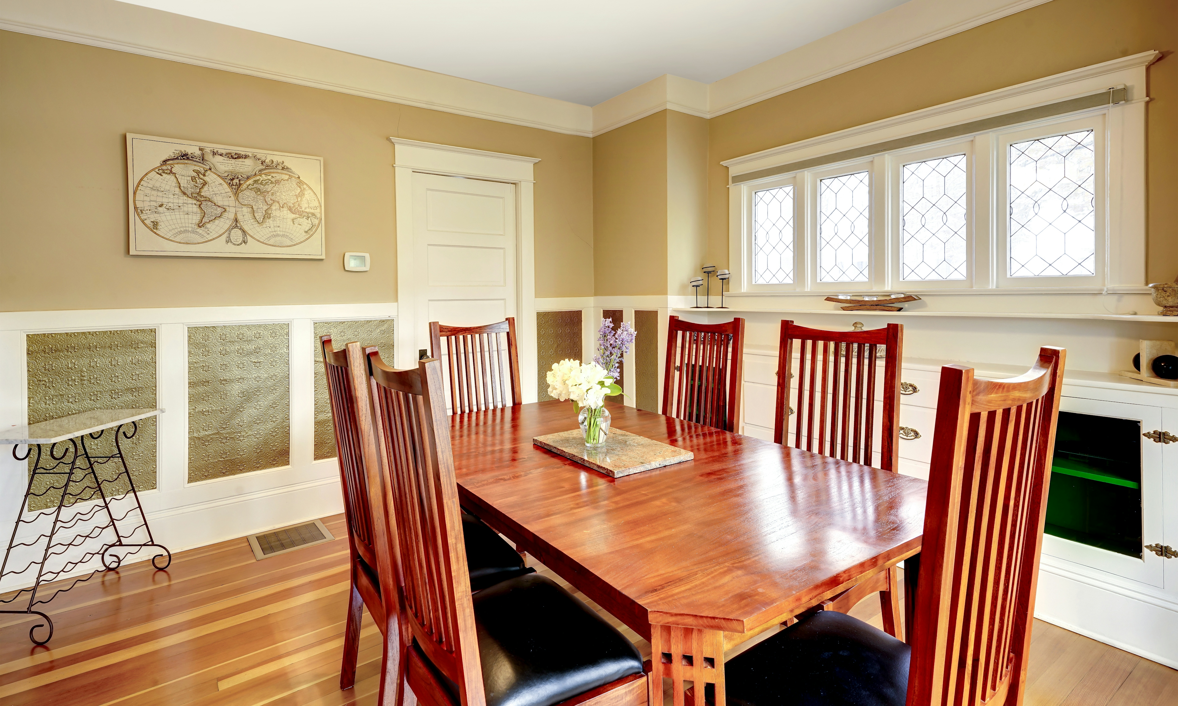 Dining room view from the interior corner showing table with 6 chairs, built in sideboard with cabinets and door to kitchen.