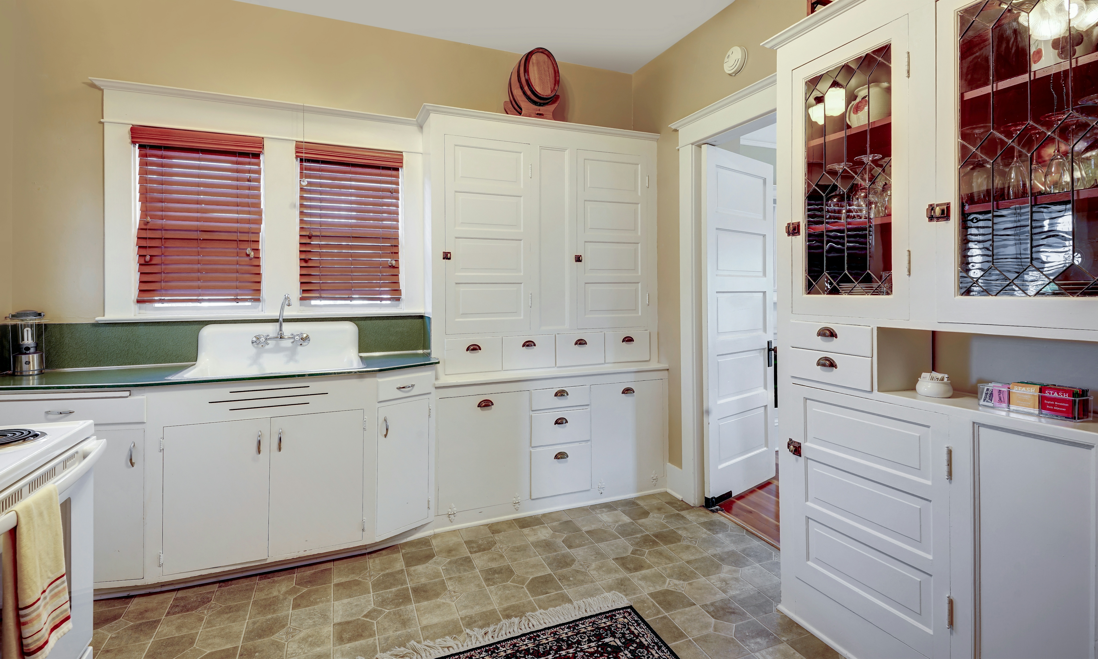 Kitchen counter, sink and built in cabinets including a built in china cabinet filled with glassware and china.