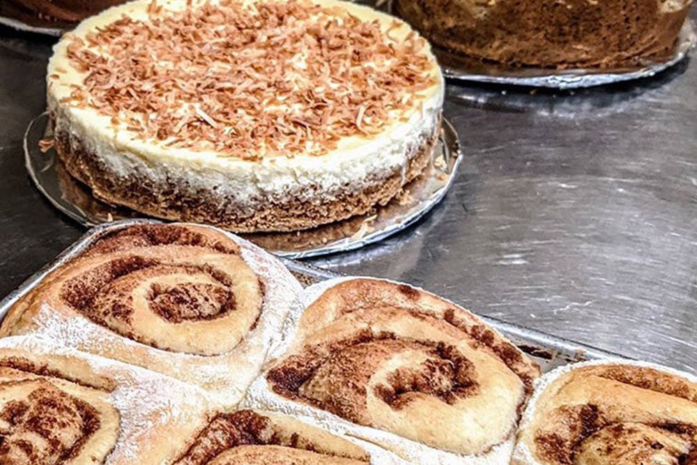 A selection of freshly baked cinnamon rolls and a toasted coconut cheesecake on a display table.