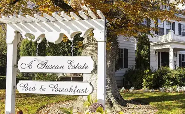 Sign for 'A Tuscan Estate Bed & Breakfast' in front of a charming house surrounded by autumn foliage.