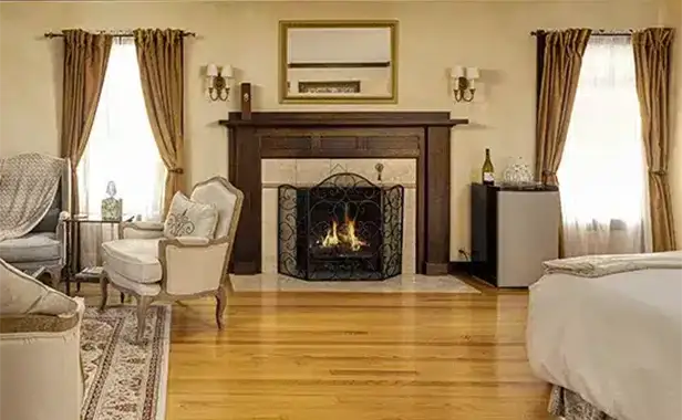 A cozy living room with a lit fireplace, elegant furniture, hardwood floors, and soft light filtering through curtained windows.