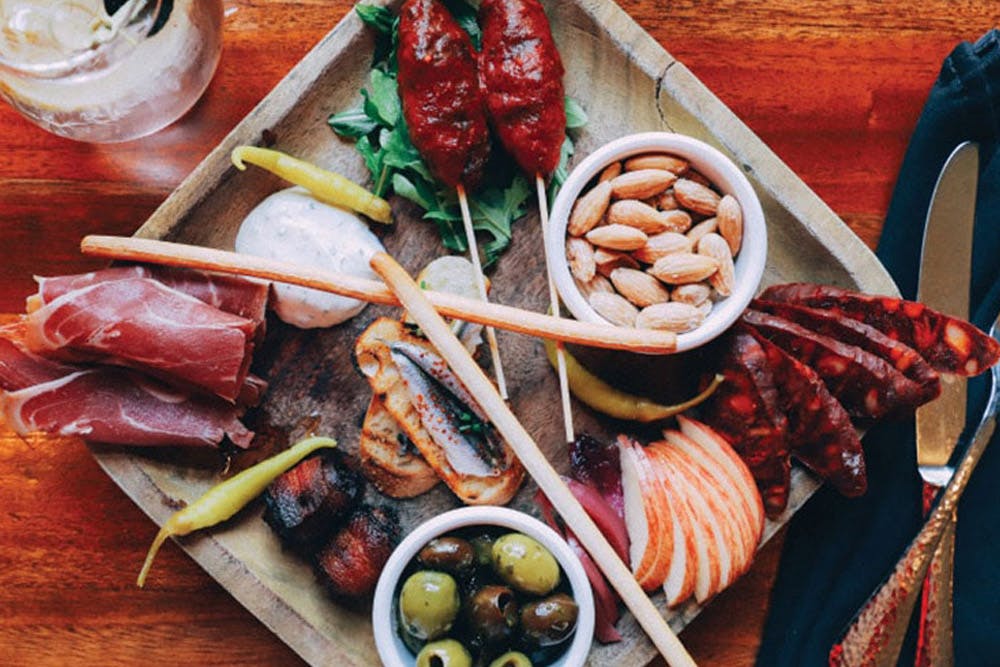 A charcuterie board featuring a variety of meats, nuts, olives, breadsticks, and cheese, artfully arranged on a wooden platter.