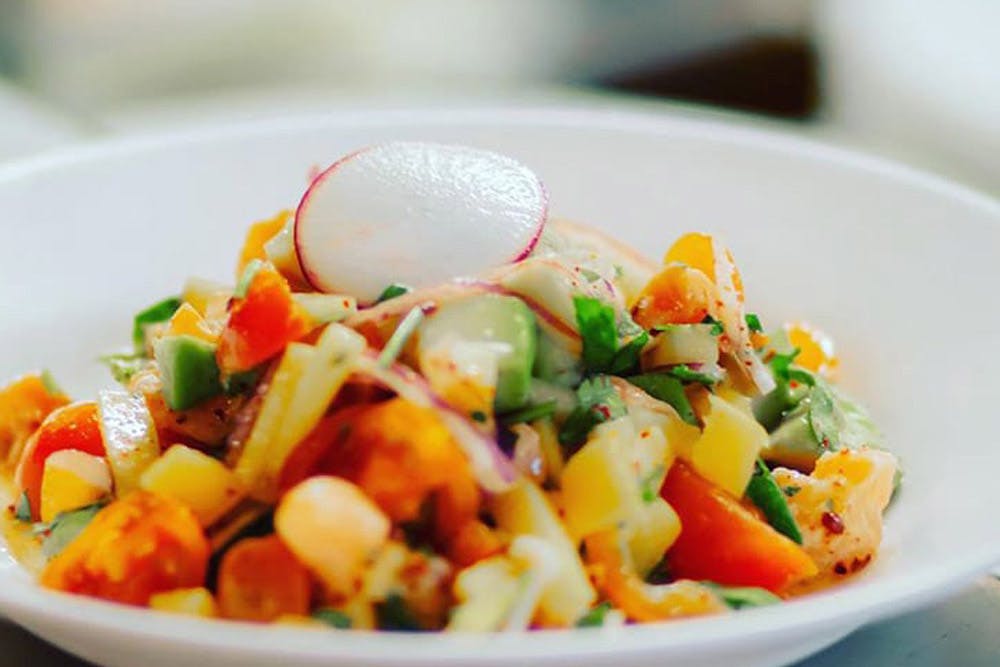 A bowl of colorful ceviche with a variety of fresh vegetables, topped with a slice of radish.