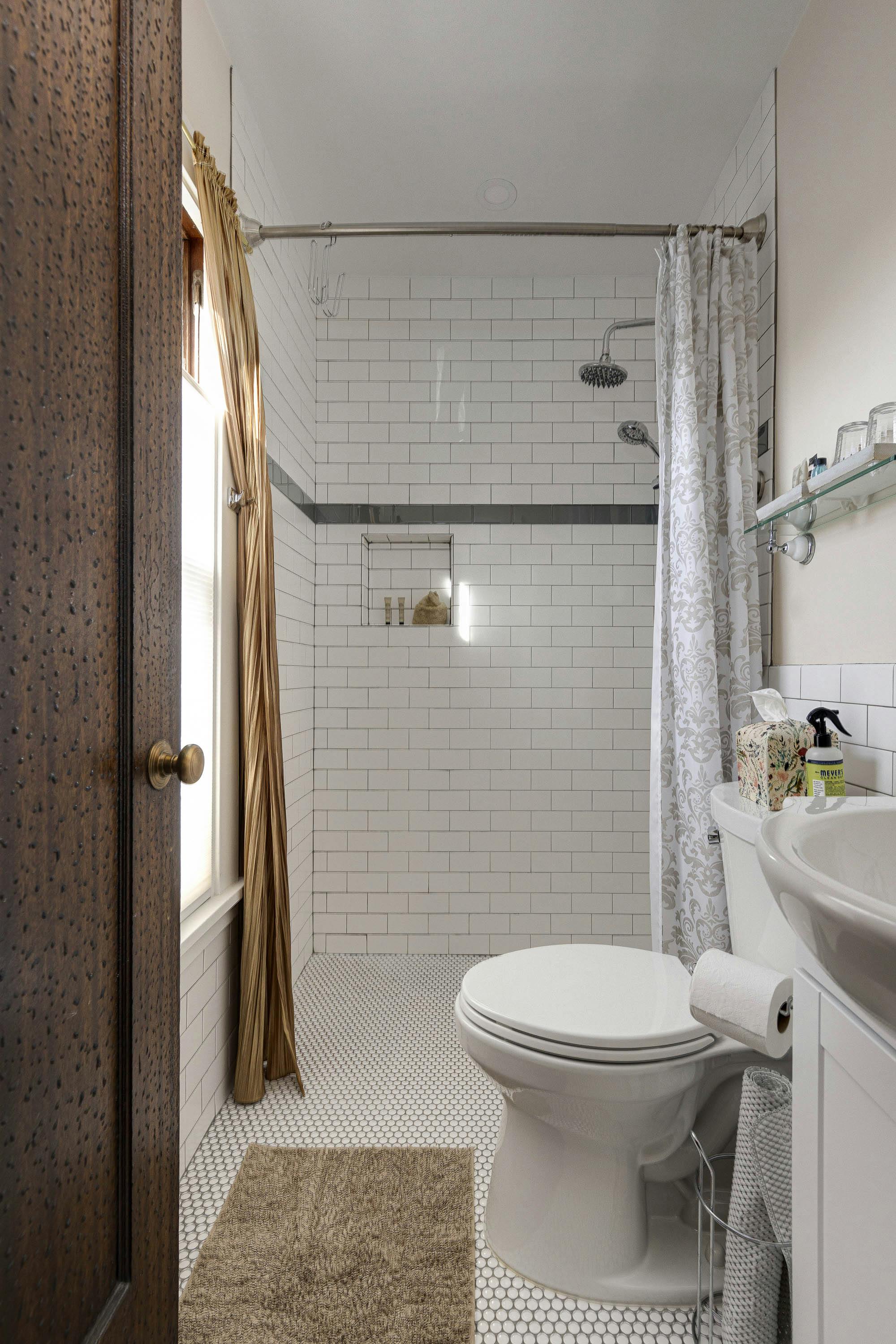 A bright bathroom with subway tiles, a white toilet, a shower area, and a glass shelf with toiletries.