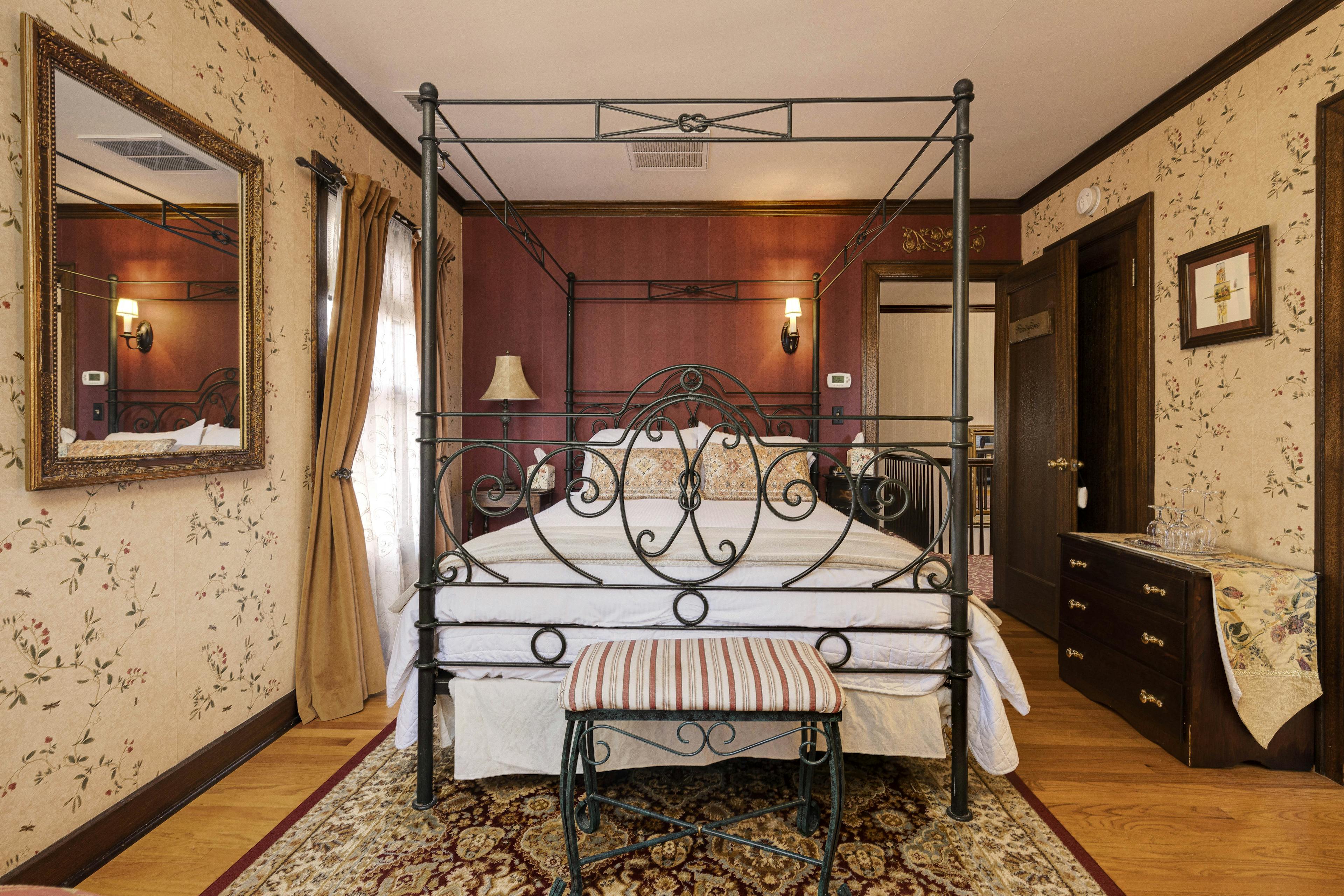 A four-poster bed with ornate ironwork in a warmly decorated room with floral wallpaper.