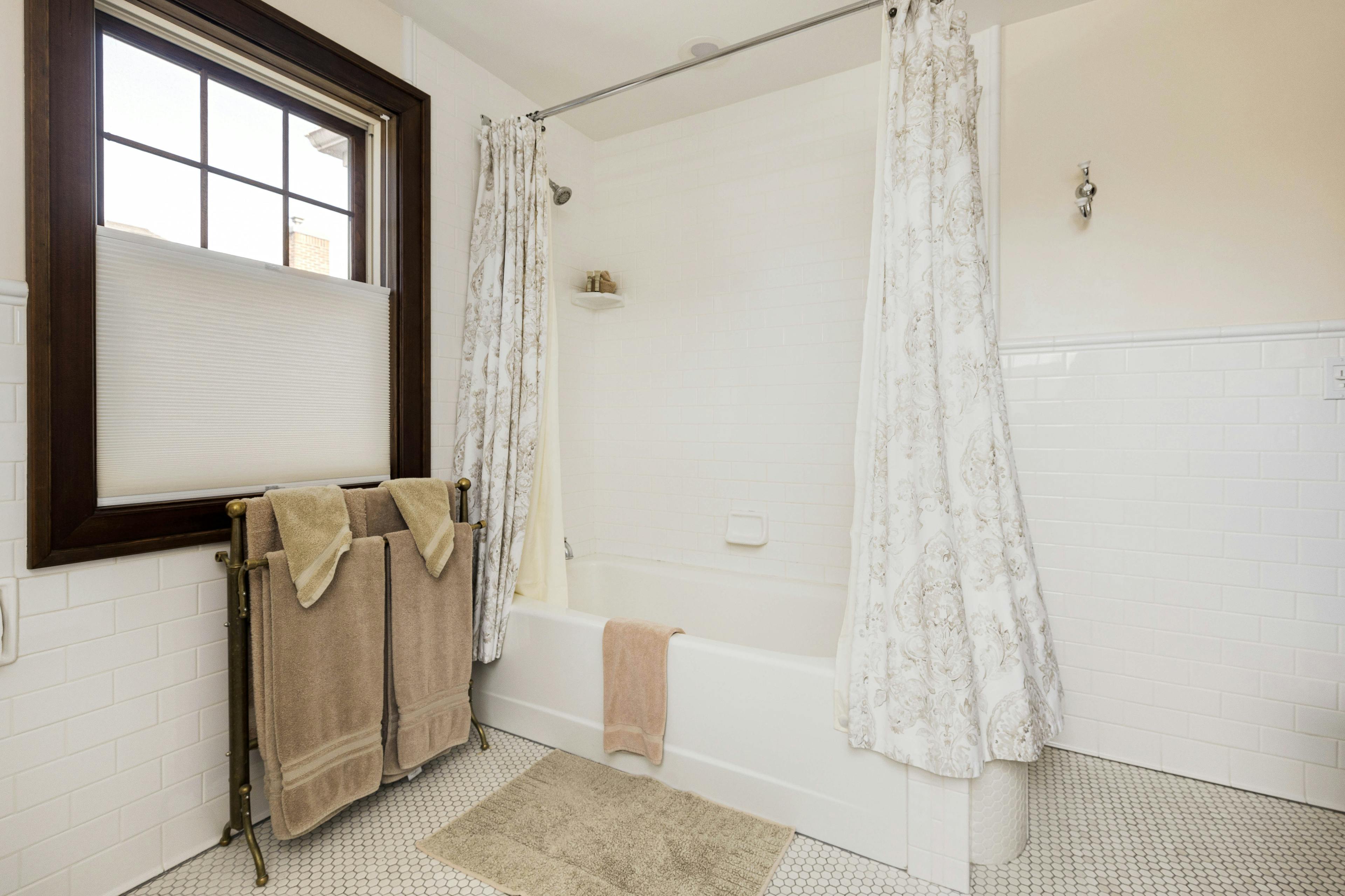 A Napoli Guest Room bathroom with a tiled shower and tub, white shower curtains, and a window.