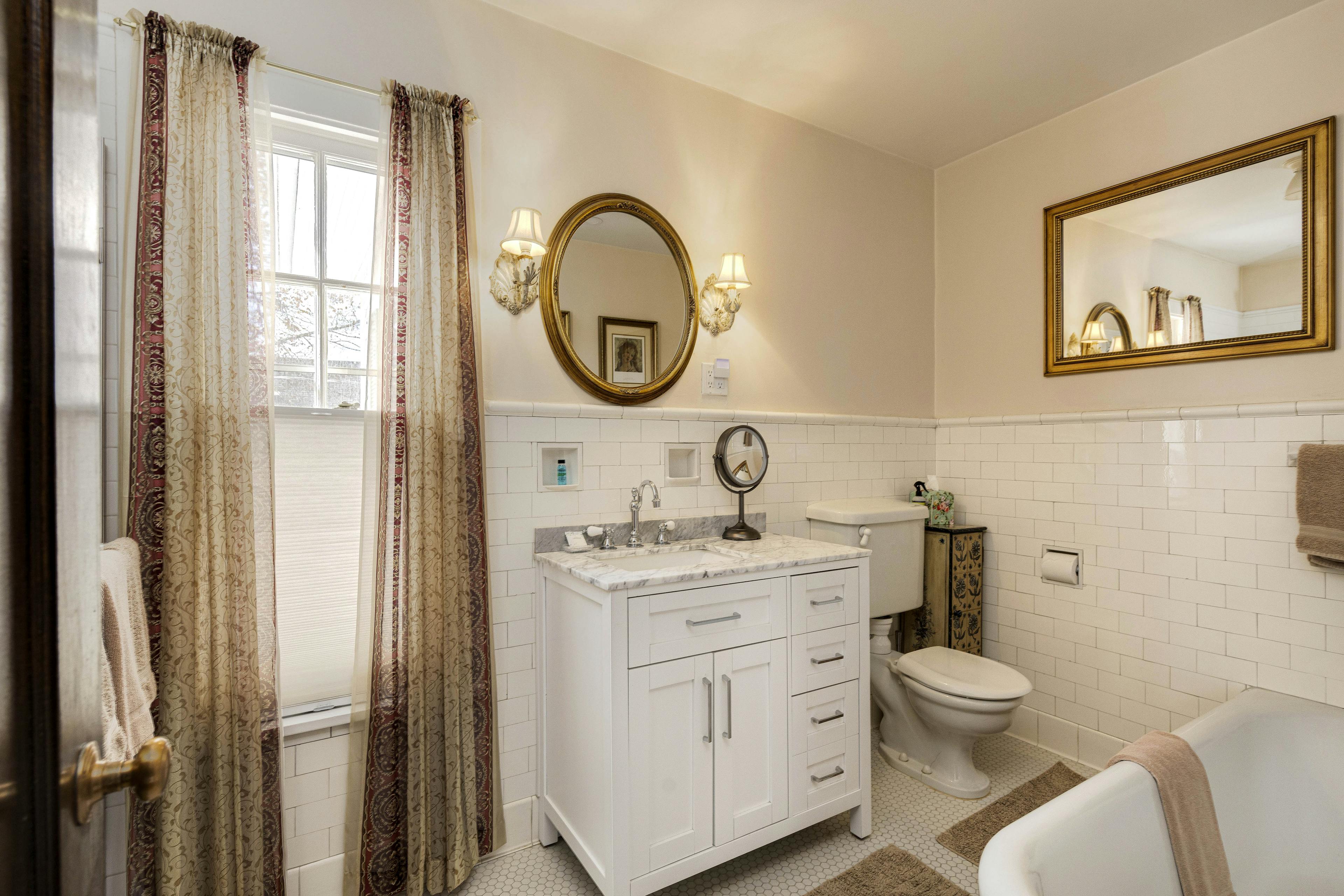 A bathroom with a white vanity, a large mirror, and bright lighting, complemented by decorative curtains.