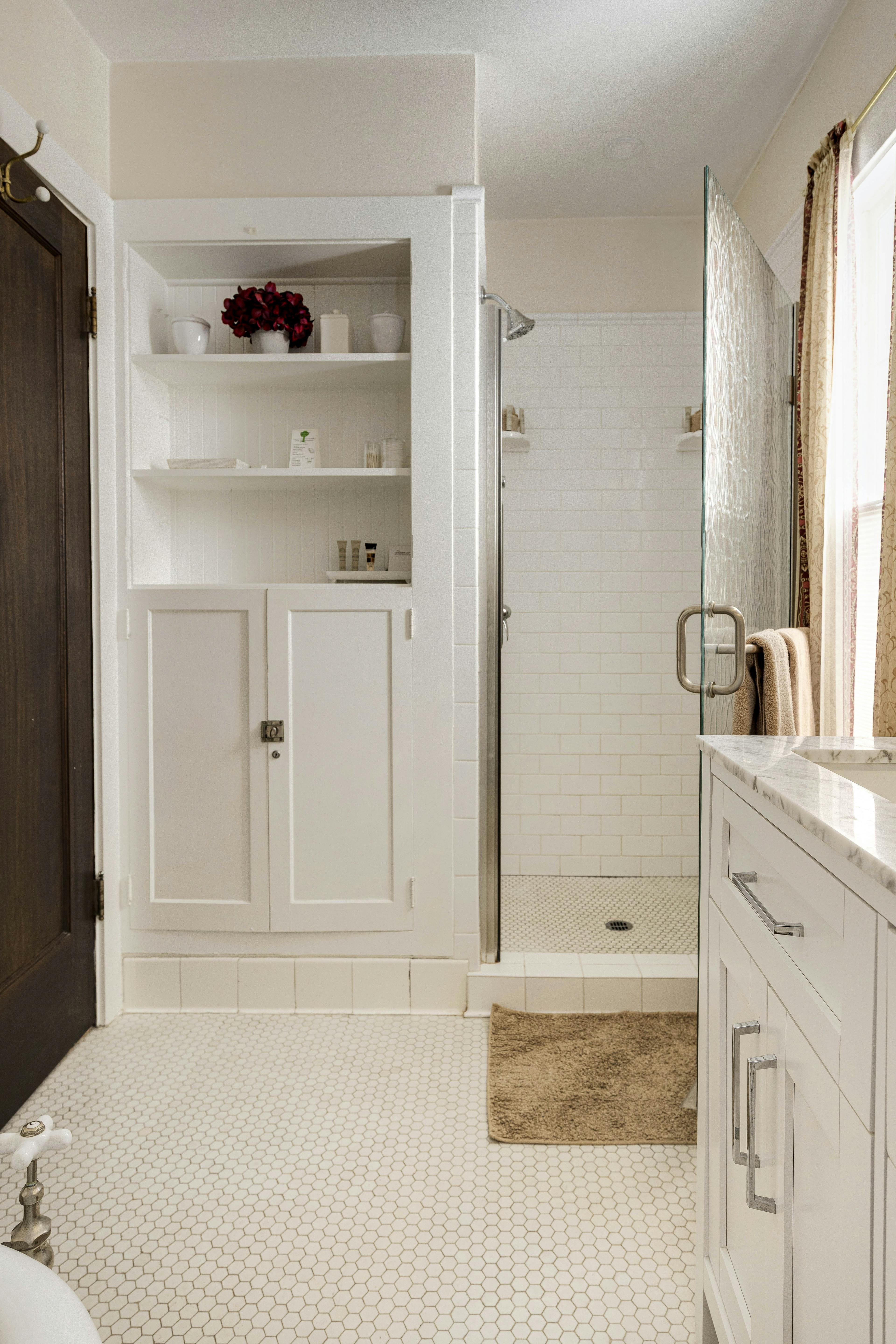 A shower area with white tiles, a glass door, and built-in shelving.