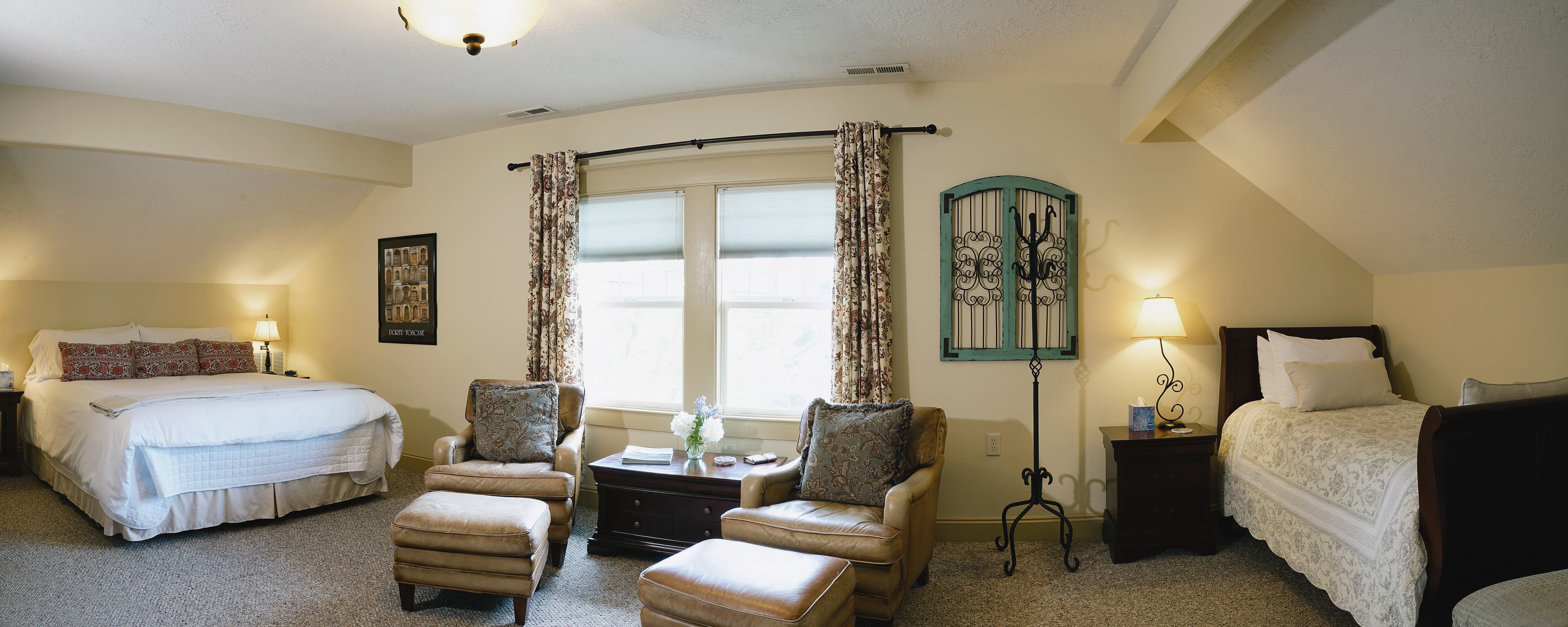 Full view of California King bed, sitting area with two club chairs and ottomans and the twin bed.