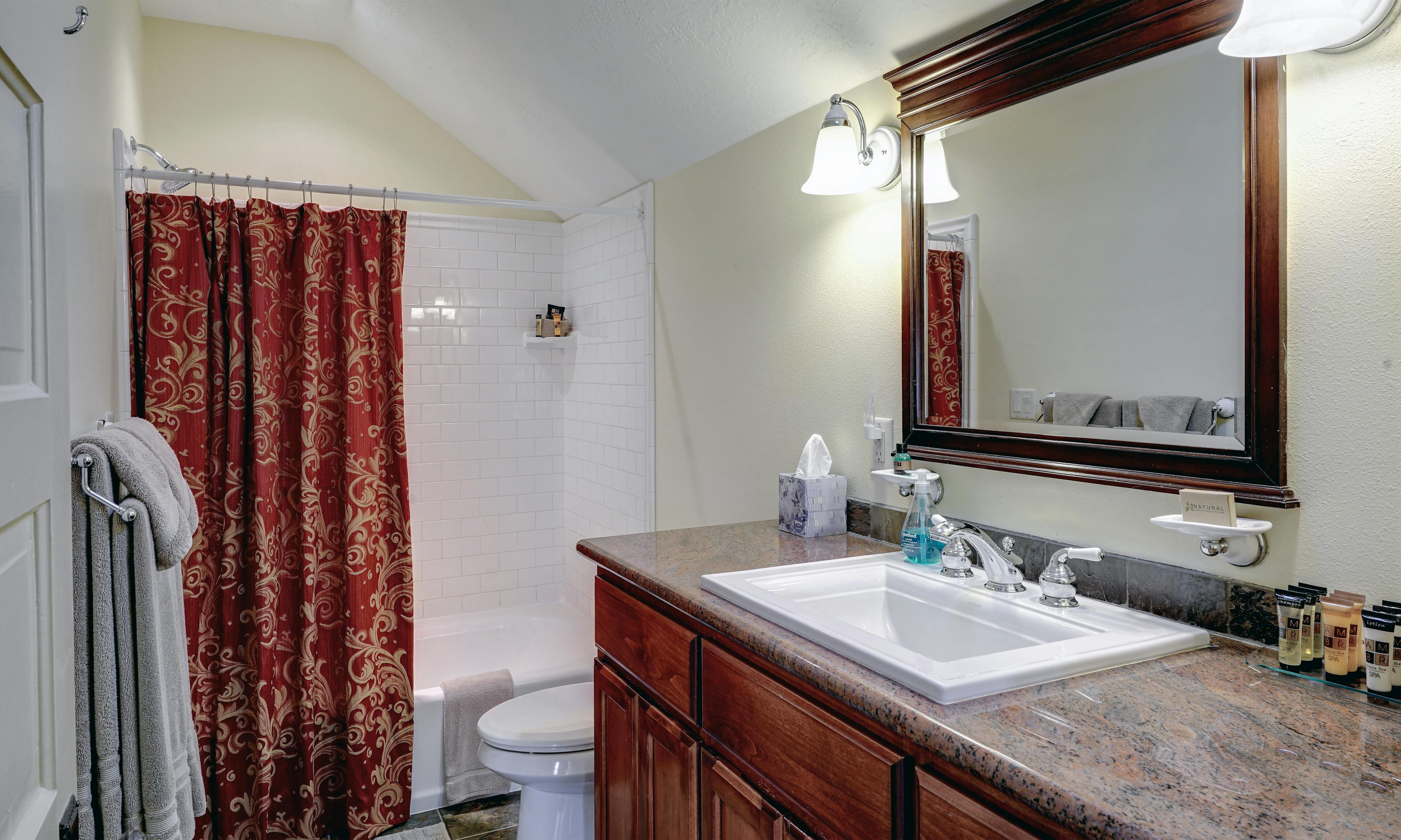 Bathroom view of shower/tub with shower curtain, toilet and granite vanity with sink.