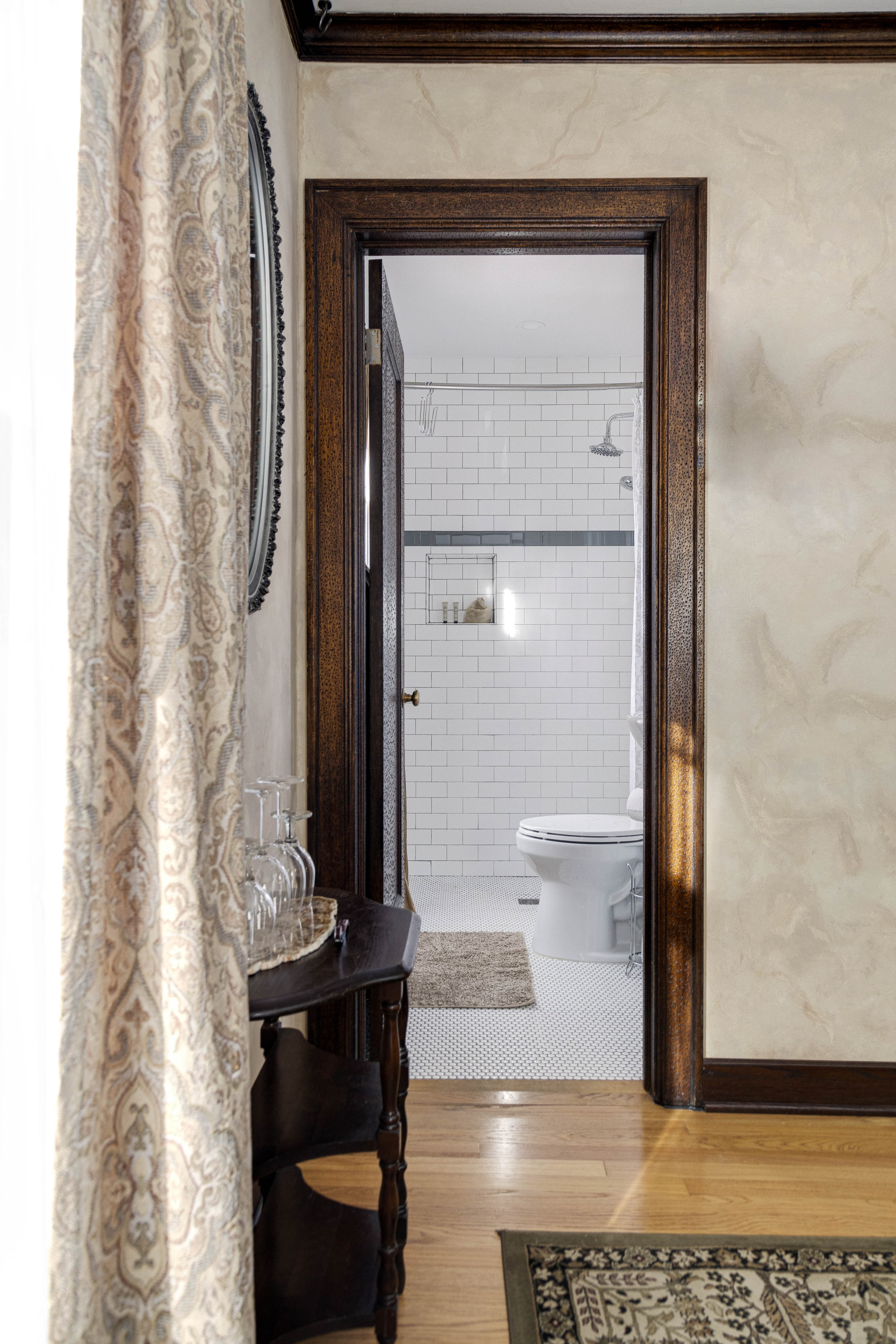 A view into a white-tiled bathroom from the guest room, with a shower and toilet visible.