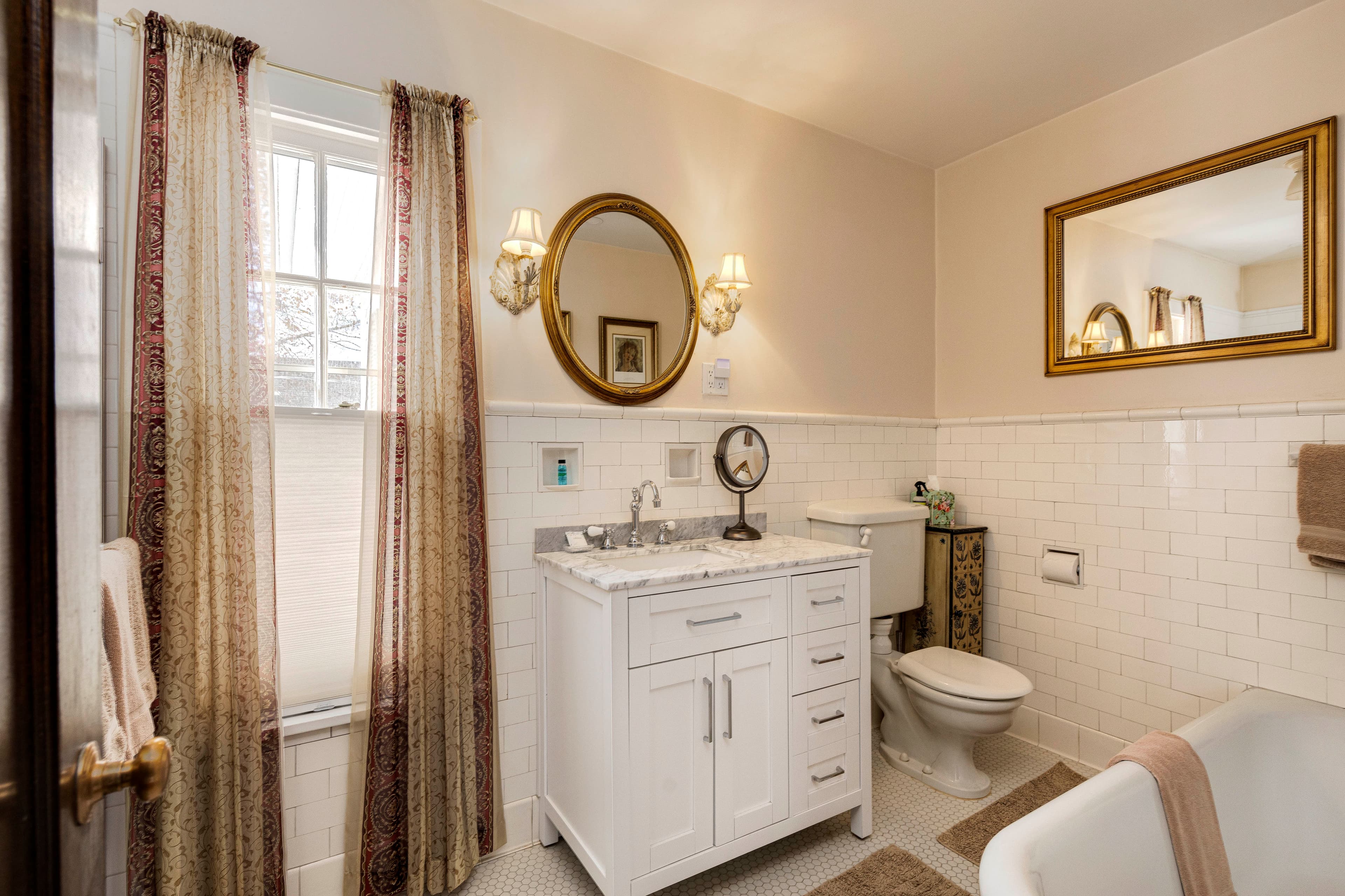 A bathroom with a white vanity, a large mirror, and bright lighting, complemented by decorative curtains.