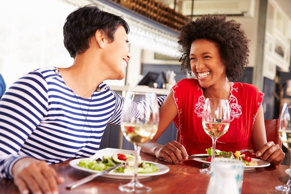 Two women enjoy a meal and share laughter in a restaurant setting.