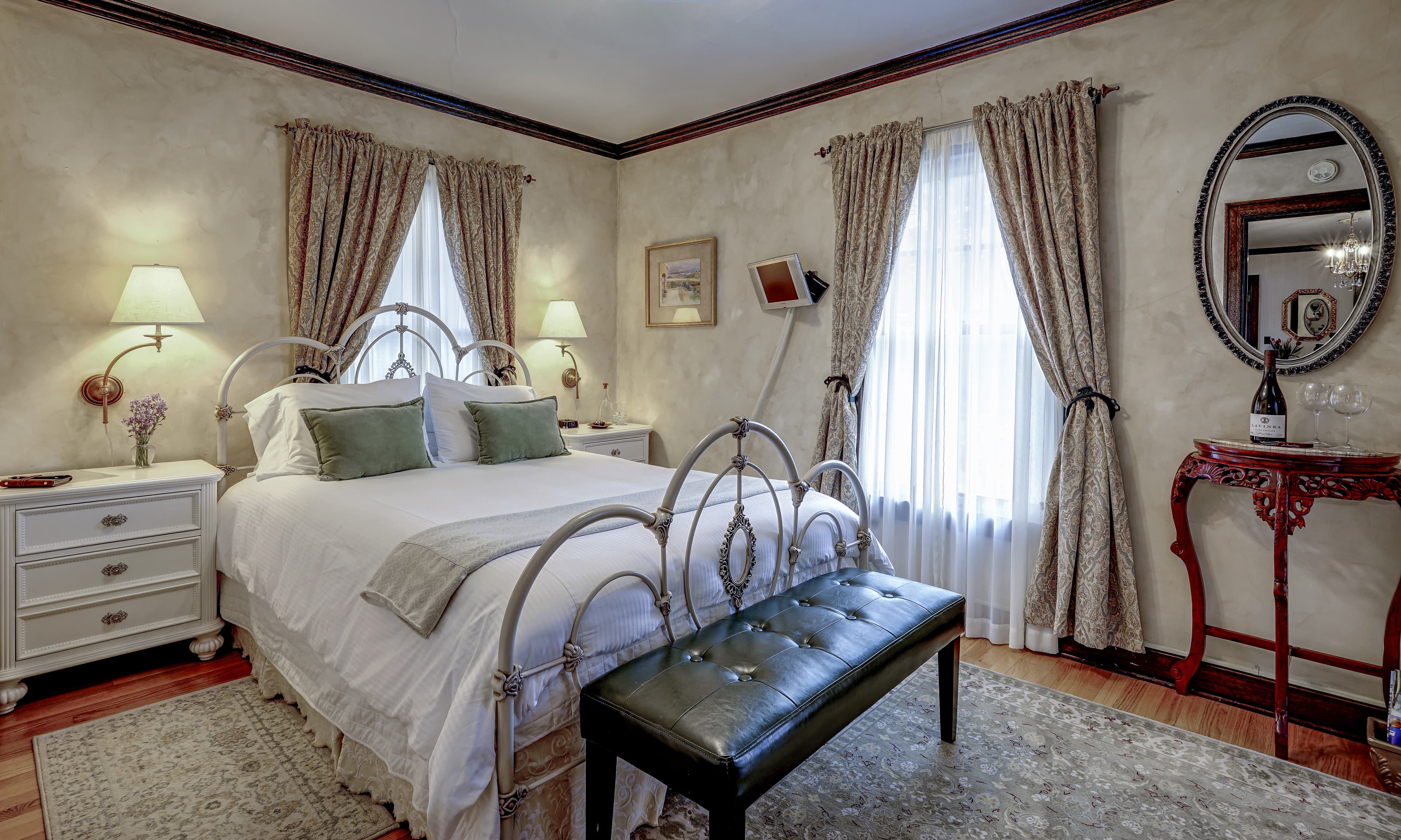 A cozy, elegantly decorated bedroom featuring a white bed with green pillows, vintage-style furnishings, and soft lighting.