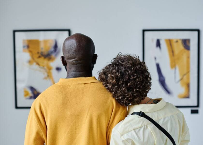 A couple stands closely together, admiring abstract art on the wall.
