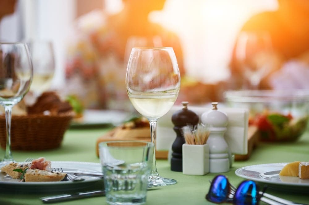 A glass of white wine sits on a table set for a meal with various dishes and condiments.