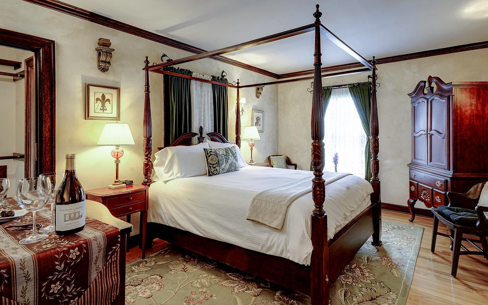A cozy bedroom featuring a four-poster bed, elegant decor, and a small table with wine glasses and a bottle.