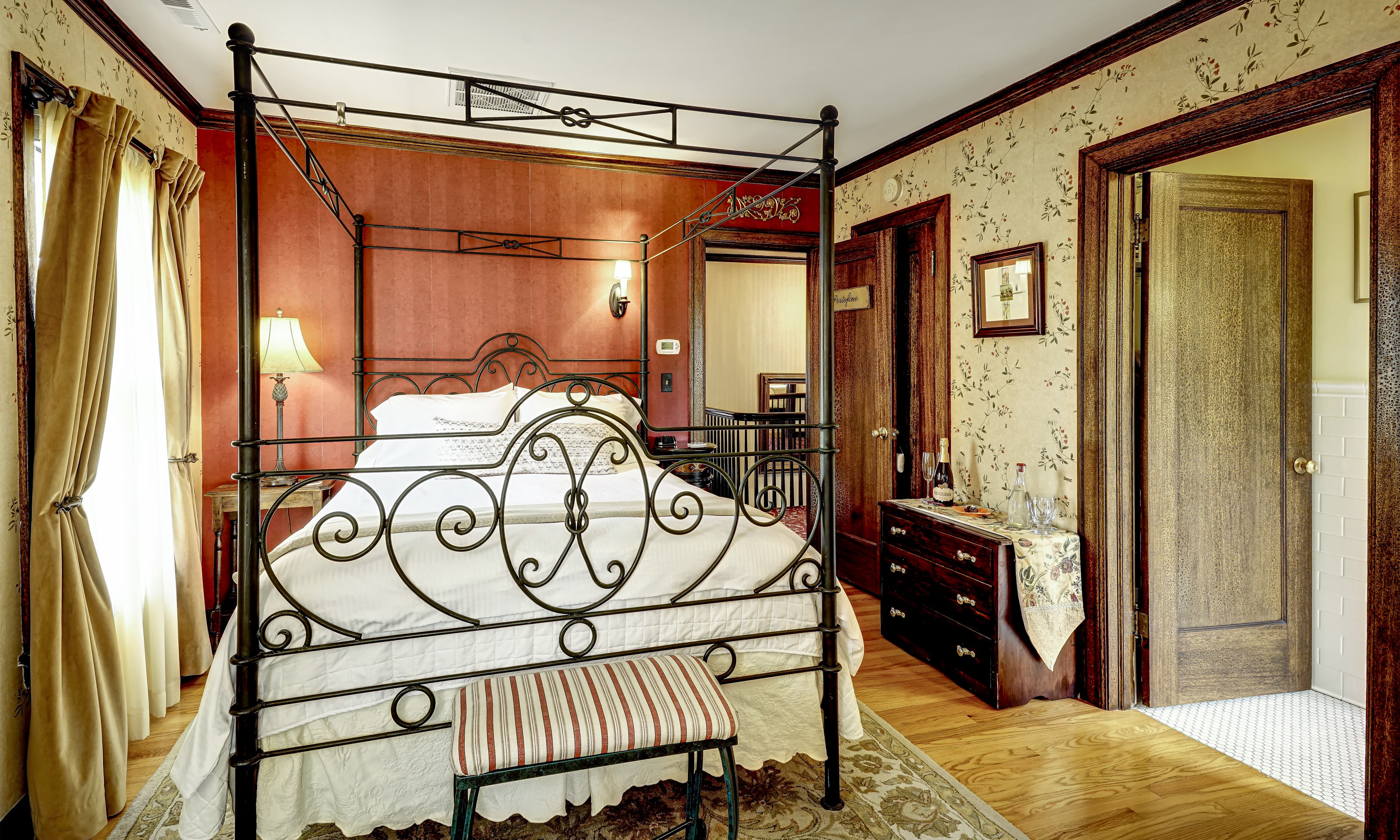 A cozy bedroom featuring a wrought iron four-poster bed, warm lighting, and floral wallpaper.