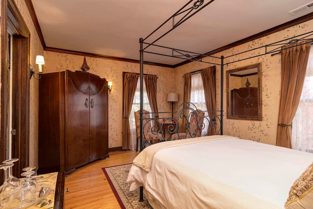 A cozy bedroom featuring a four-poster bed, vintage furniture, and floral wallpaper.