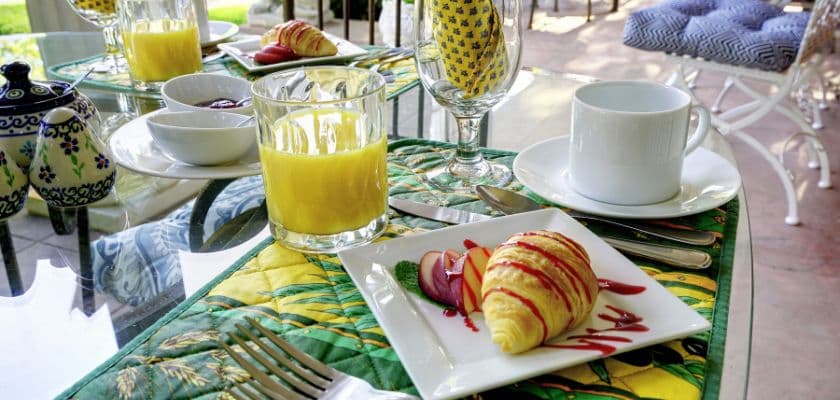 A beautifully arranged breakfast table featuring a croissant, fresh fruit, orange juice, and coffee on a colorful tablecloth.