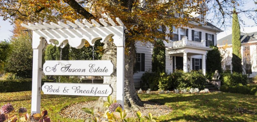 A charming bed and breakfast sign in front of a historic white house surrounded by autumn foliage.