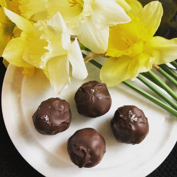 A plate of chocolate truffles with a sprinkle of salt, surrounded by yellow daffodils.