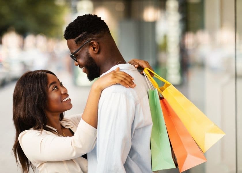 A couple share a joyful moment while holding shopping bags outside. A couple share a joyful moment while holding shopping bags outside.