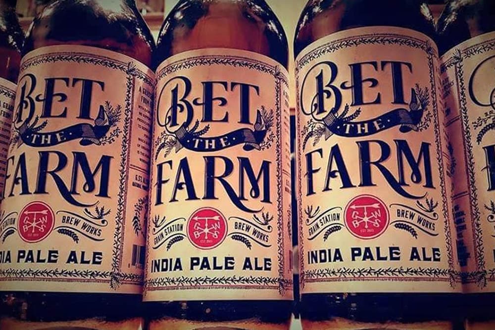 A close-up of multiple bottles of "Bet the Farm" India Pale Ale with decorative labels.