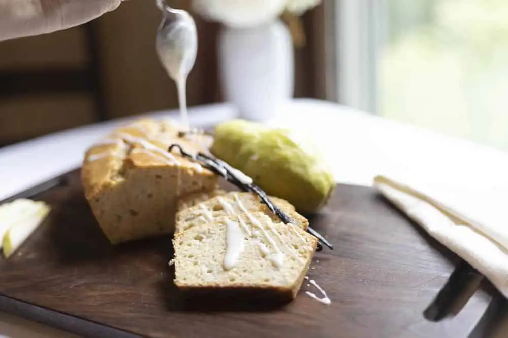 A slice of cake drizzled with icing on a wooden cutting board.