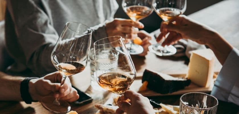 Cheers with wine glasses over a wooden table topped with cheese.