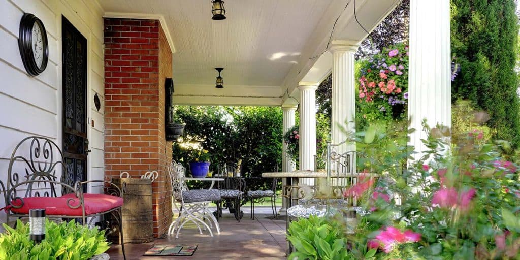 A serene porch with decorative seating, potted plants, and blooming flowers.