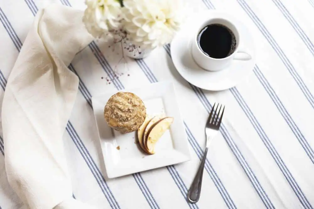 Coffee, a muffin, and apple slices on a striped tablecloth.