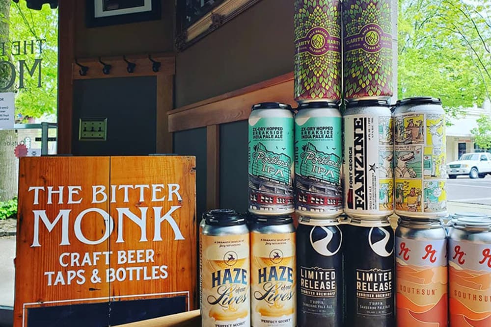 A display of various craft beer cans next to a wooden sign for "The Bitter Monk."