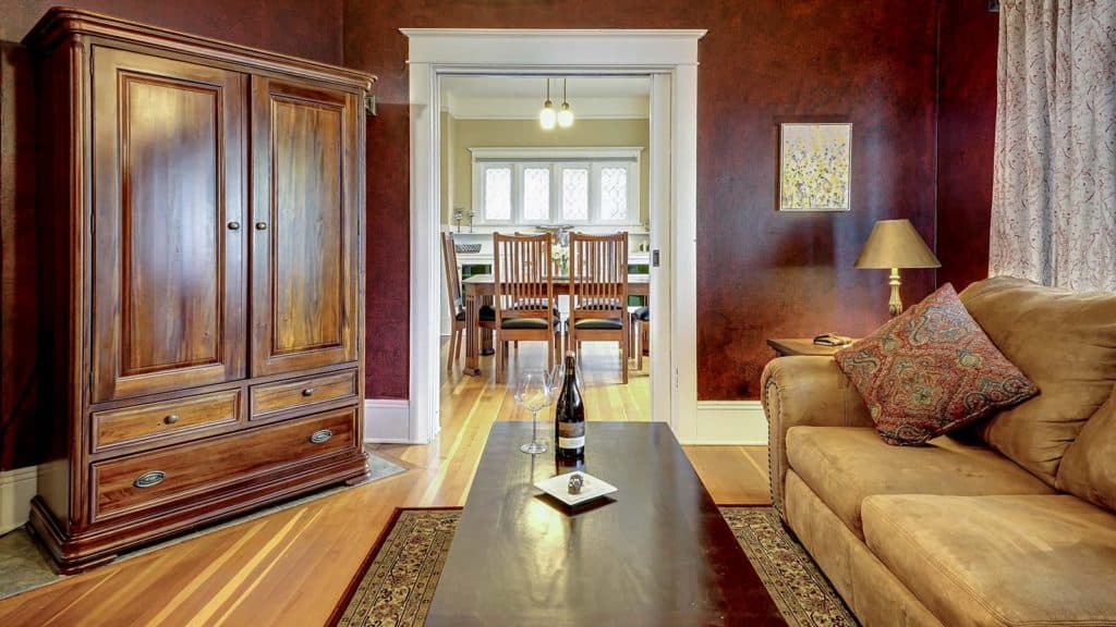 A cozy living room with a wooden armoire, a sofa, and a dining area visible through an open doorway.