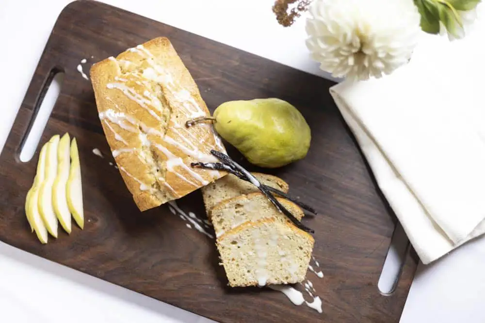 Sliced vanilla pear bread with a pear and apple slices on a wooden cutting board.