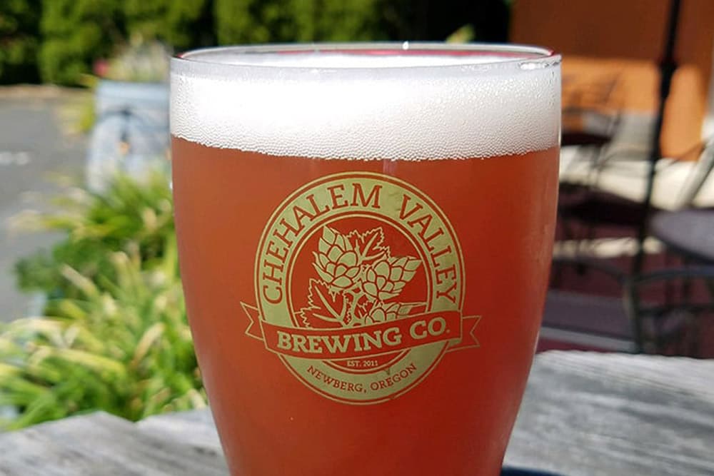A glass of amber beer with the Chehalem Valley Brewing Co. logo on a rustic table.