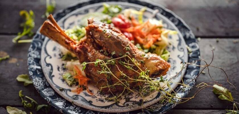 A succulent roasted meat leg served on an ornate plate with fresh salad garnish.
