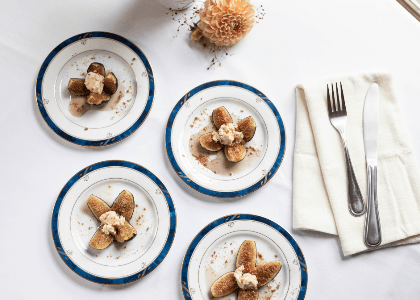 Four plates of sliced figs topped with cream, arranged on a table with cutlery and a floral centerpiece. Four plates of sliced figs topped with cream, arranged on a table with cutlery and a floral centerpiece.