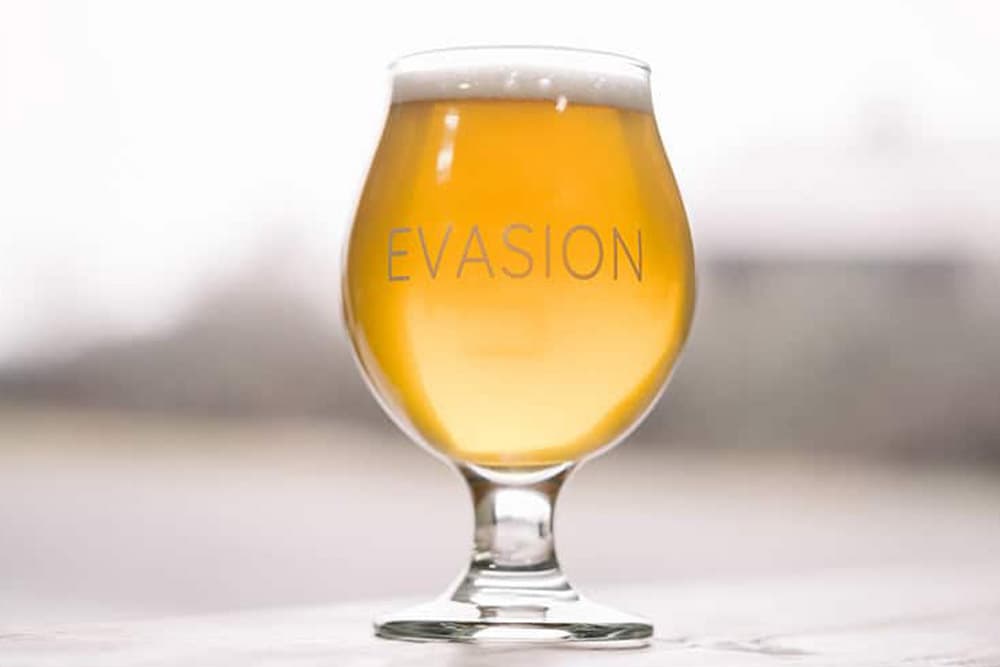 A glass of golden beer with the word "EVASION" etched on it.