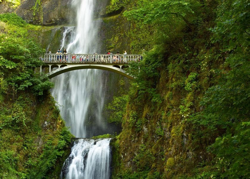 A waterfall cascades down rocky cliffs, with a bridge above where people gather. A waterfall cascades down rocky cliffs, with a bridge above where people gather.