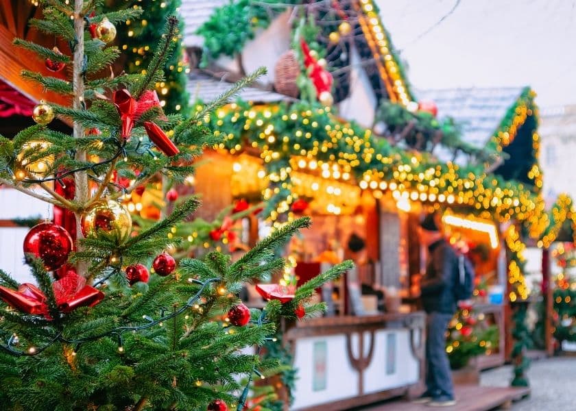 decorated christmas tree with red ornaments and lights in front of festive holiday market stalls decorated christmas tree with red ornaments and lights in front of festive holiday market stalls