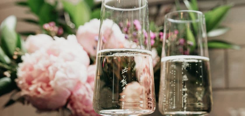 Two wine glasses filled with sparkling white wine and with pink flowers in the background.