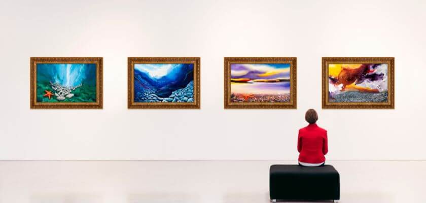 a person seated on a bench in an art gallery viewing paintings hanging on the wall