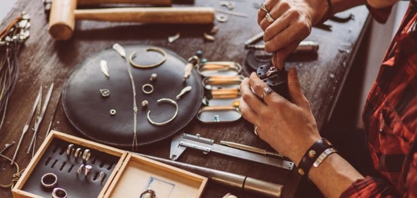 artisan works at a table with tools and jewelry pieces, creating handcrafted jewelry