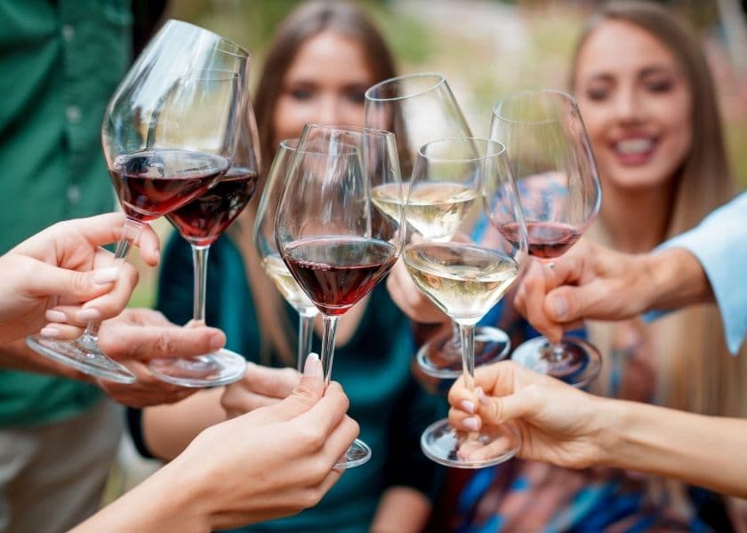 close-up of a group raising glasses of red and white wine in celebration outdoors
